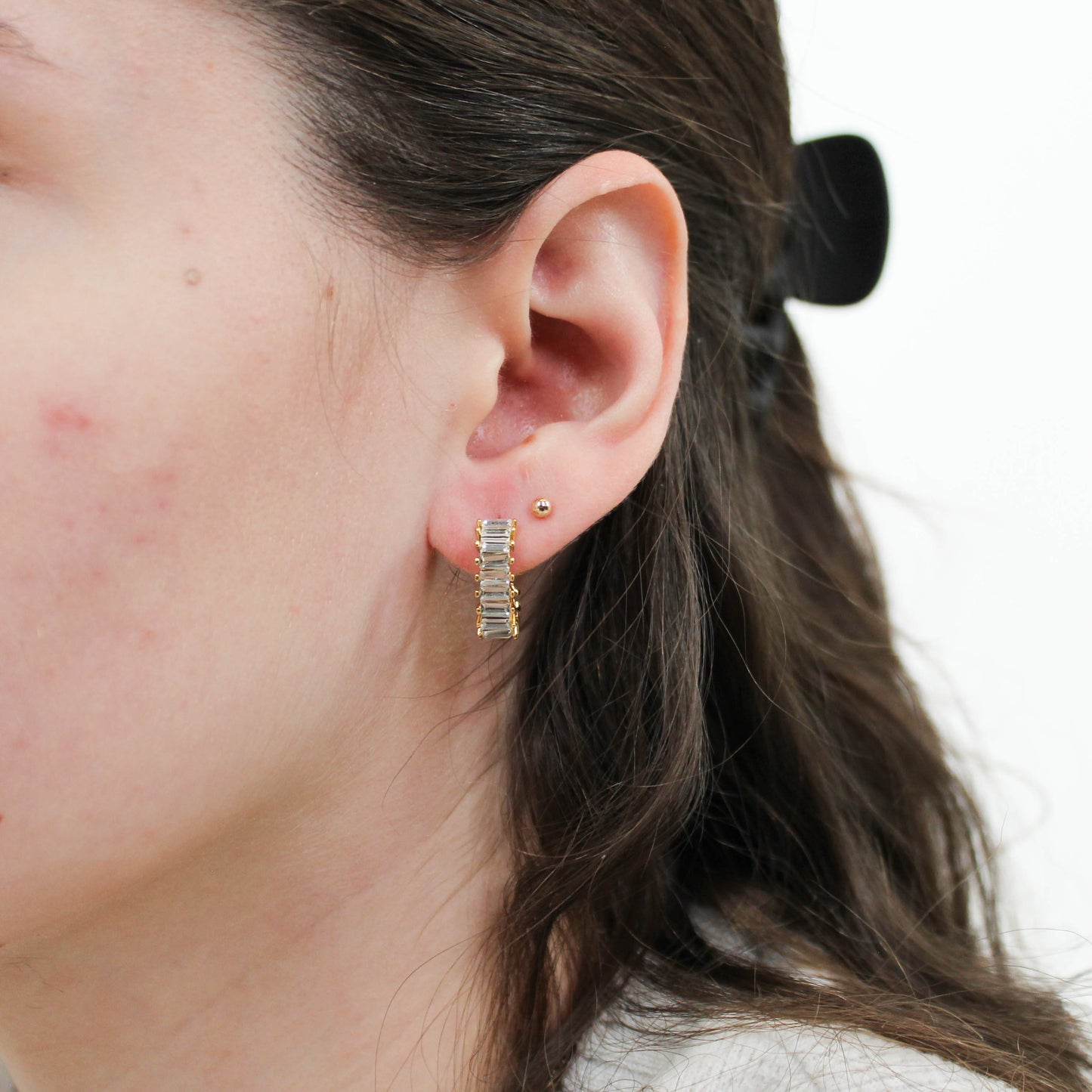 Close-up of an ear wearing gold clear stone stainless earrings with a white background