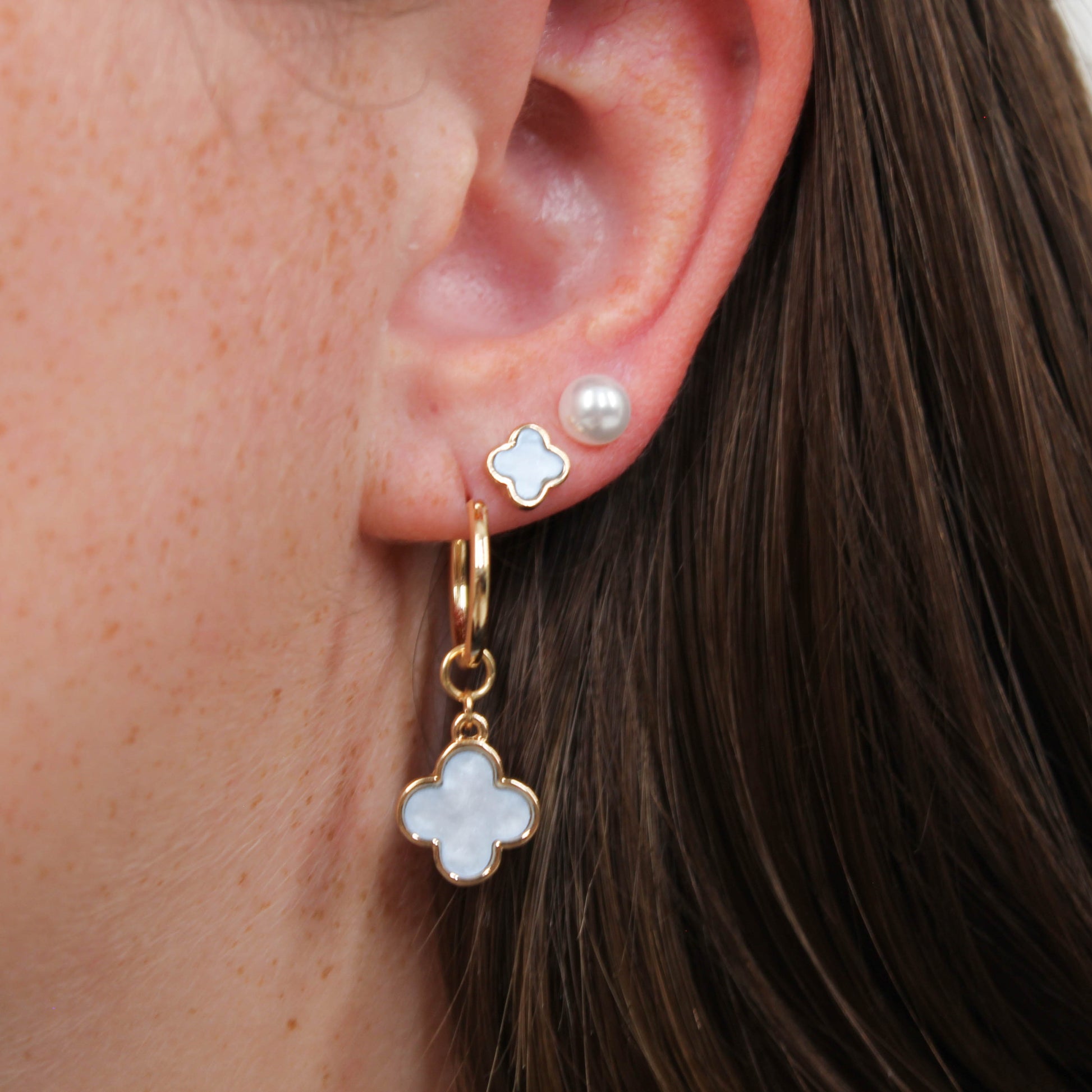 Close-up of an ear with gold clover earring set in white