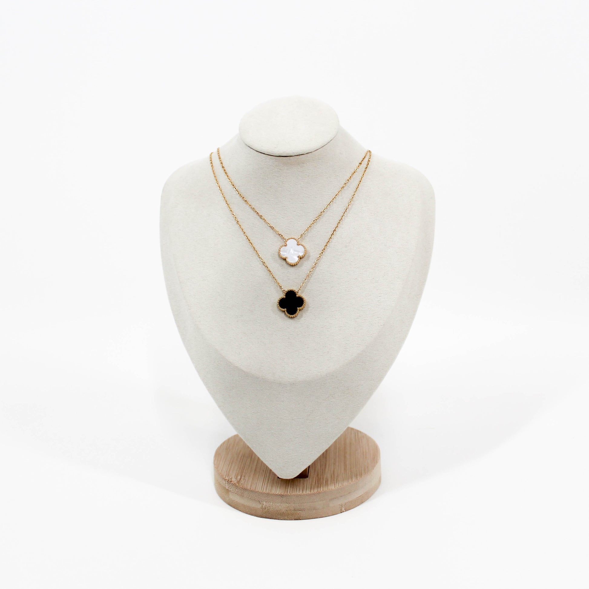 Two gold clover pendant necklaces on a white mannequin bust with a white background