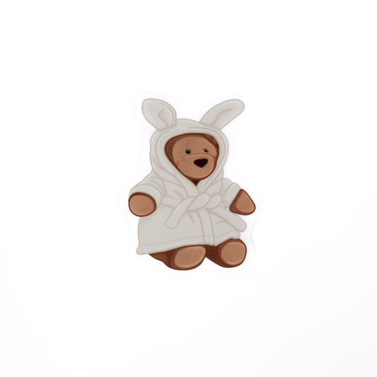 Teddy bear toy wearing a white robe with bunny ears on a white background