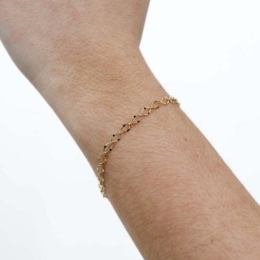 Gold diamond cut chain bracelet on a person's wrist against a white background