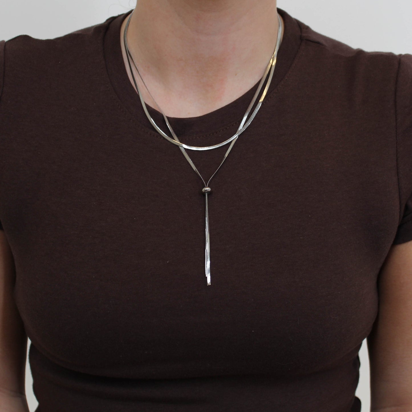 Person wearing a silver double loop lariat necklace featuring a long, thin pendant.