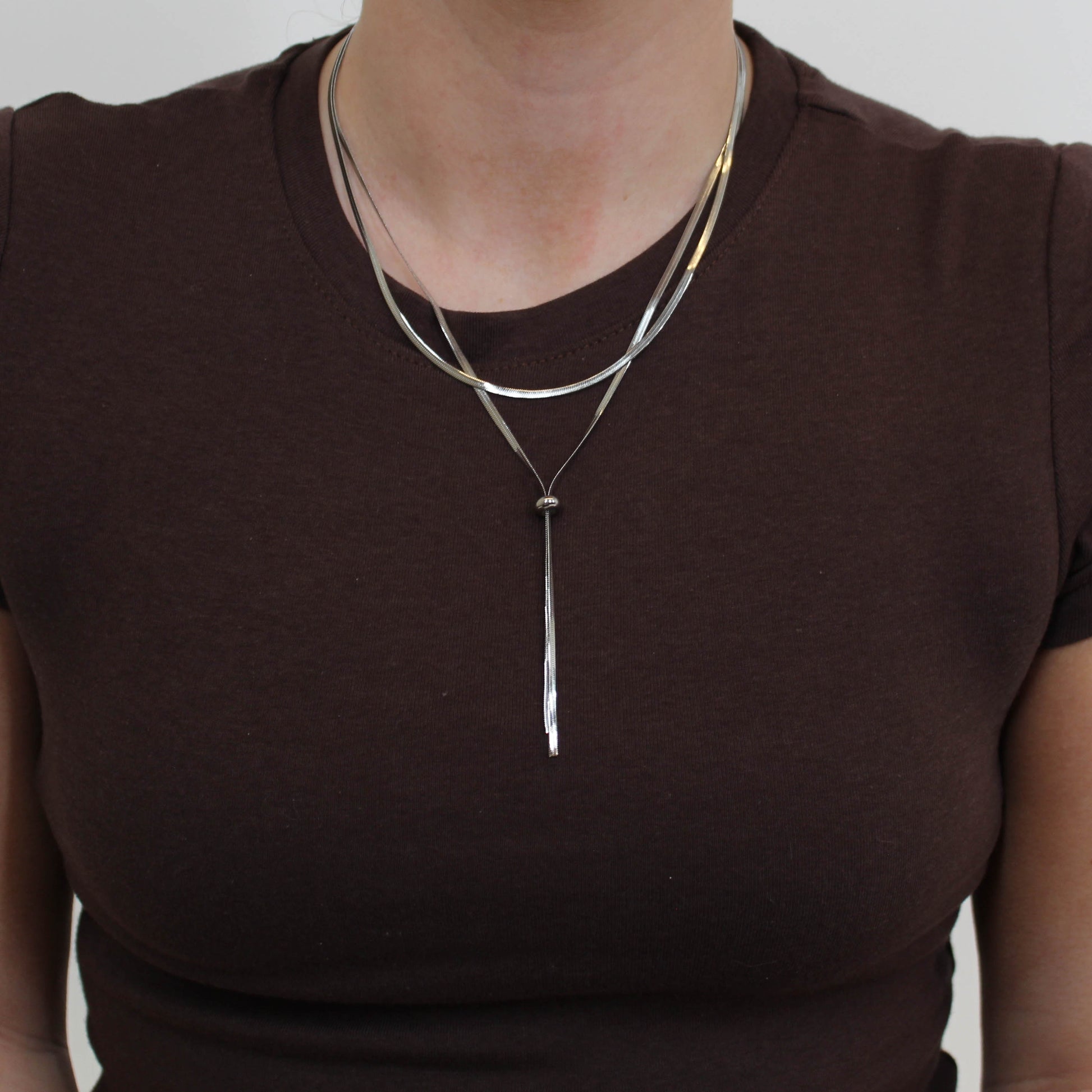 Person wearing a silver double loop lariat necklace featuring a long, thin pendant.