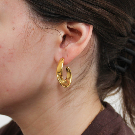 a person wearing gold geometric hoop earrings.