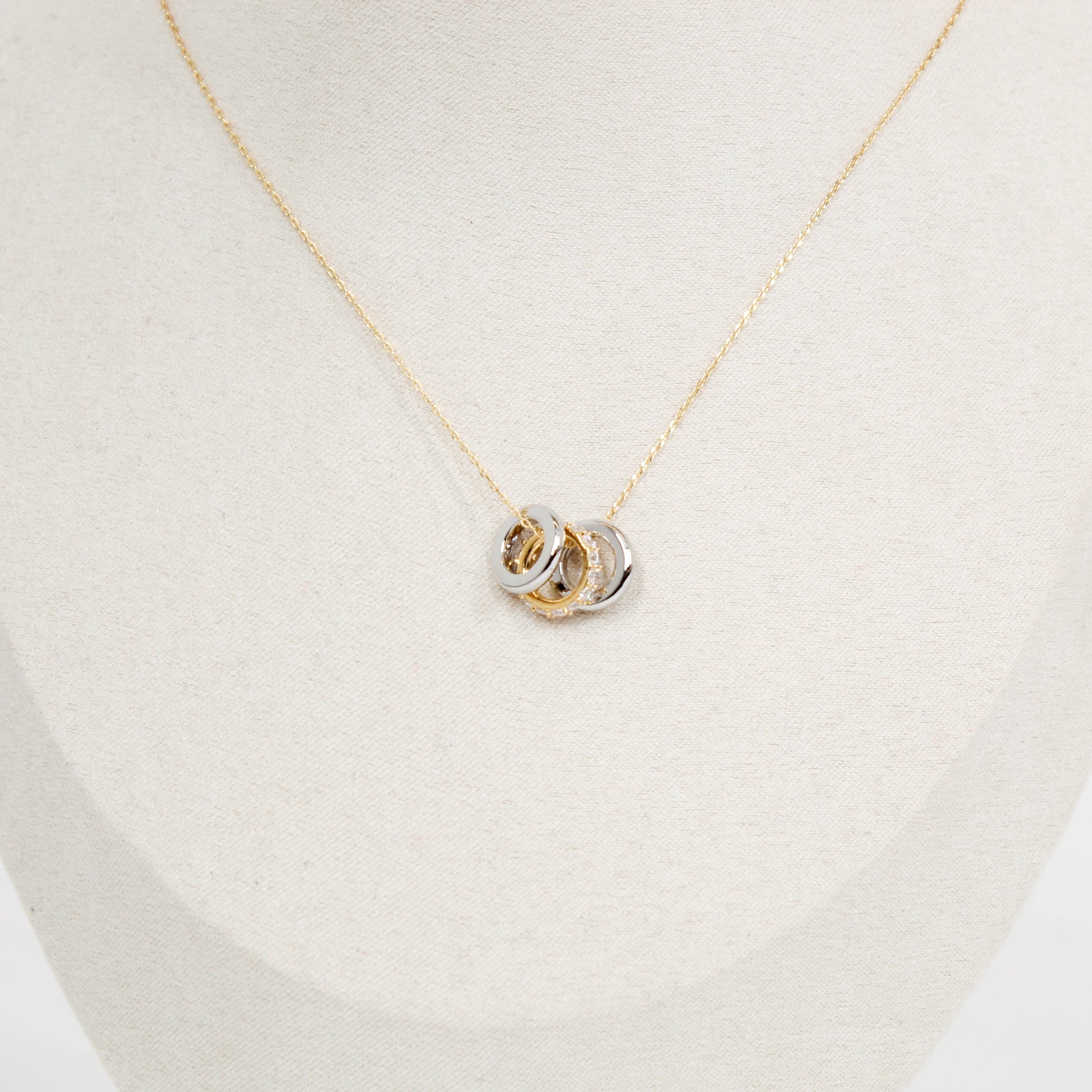 Gold necklace with a three ring pendant on a light beige background