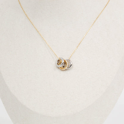Gold necklace with a three ring pendant on a light beige background