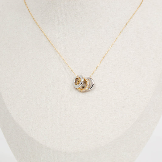 Gold necklace with a three ring pendant on a light beige background