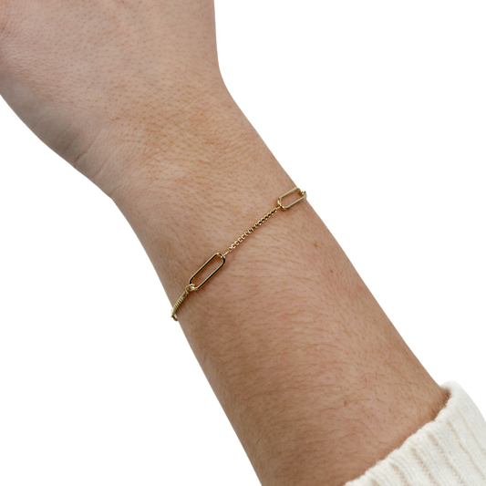 Gold chain link bracelet on a wrist with a white background