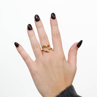 Hand wearing a gold halo heart ring on a white background