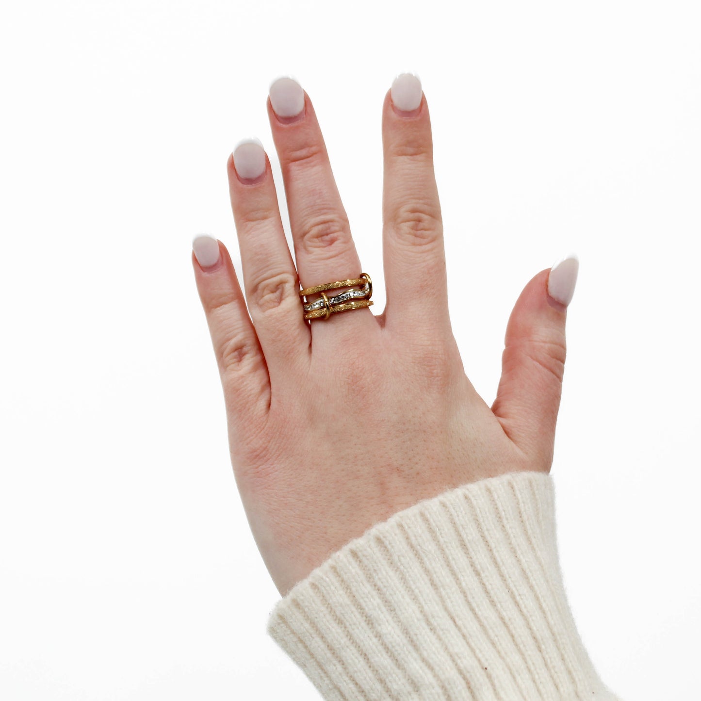 Hand wearing a gold and silver interlocking link ring with a white background