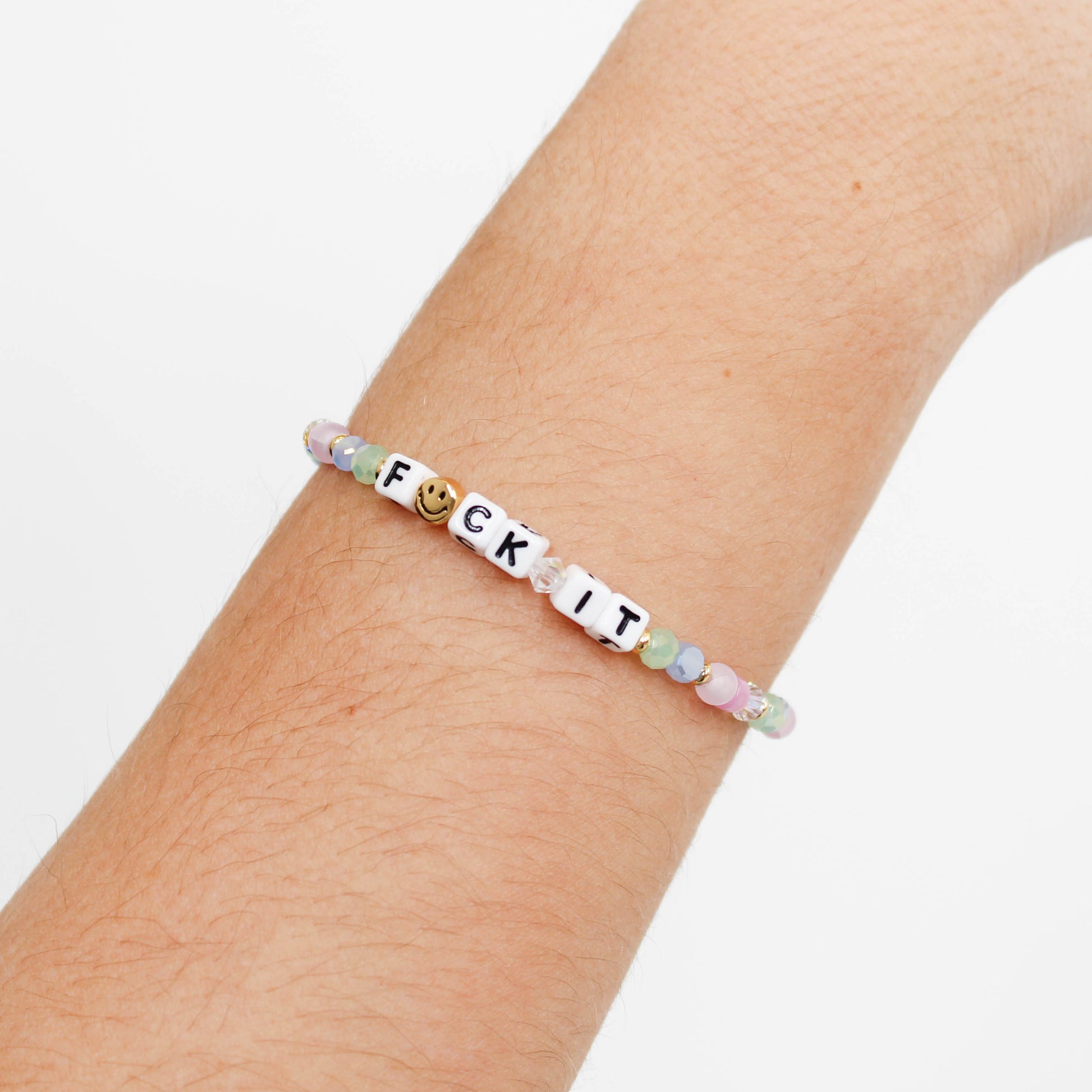 Bracelet with letter beads spelling 'F*CK IT' on a wrist against a white background