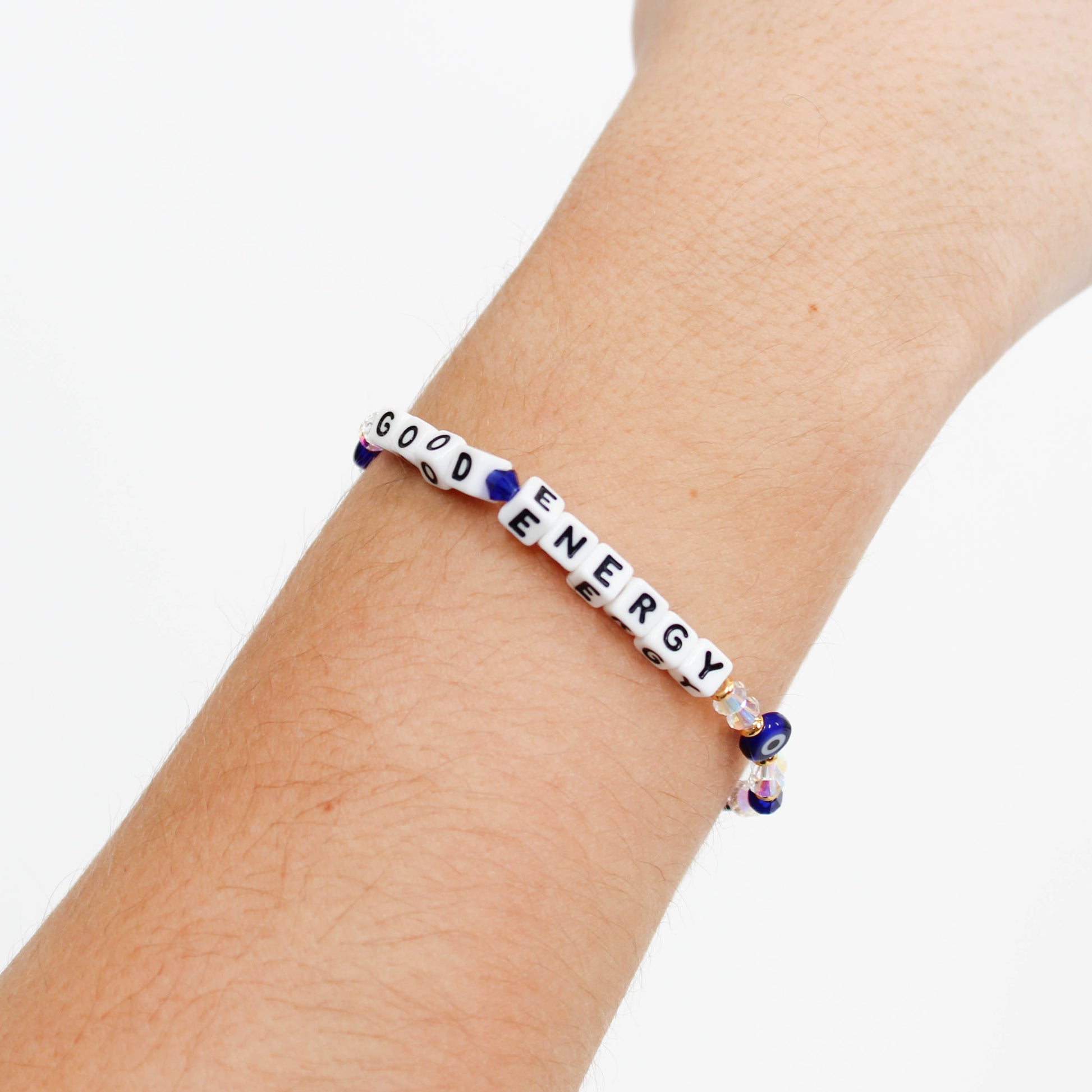 Little Words Project bracelet with "good energy" message on wrist and evil eye beads against a white background