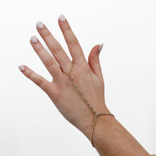 Hand wearing a gold marquise hand chain bracelet on a white background