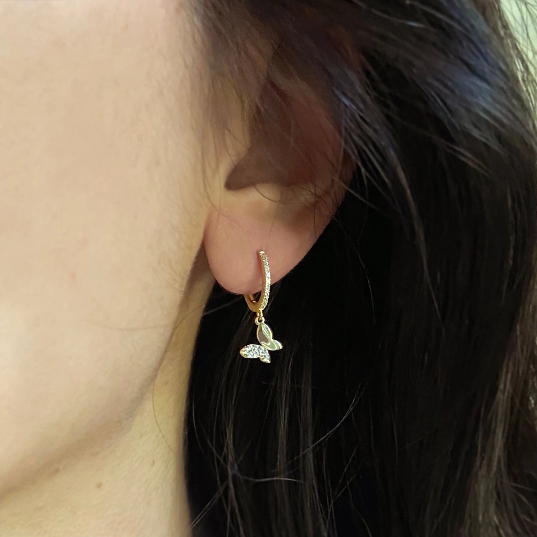 Gold hoop earring with a butterfly charm worn by a person.