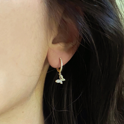 Gold hoop earring with a butterfly charm worn by a person.
