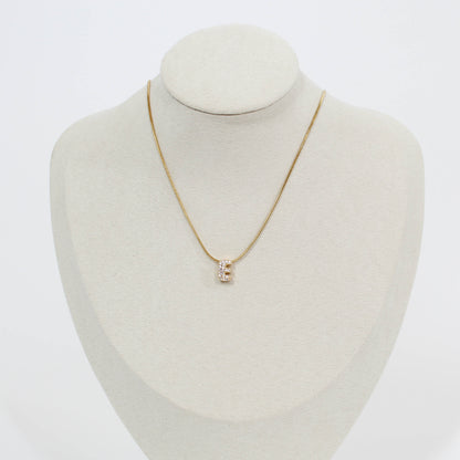 Gold necklace with an E pendant on a mannequin bust against a white background