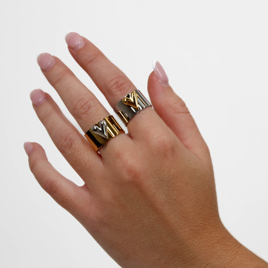 Hand wearing two mixed metal heart rings on a plain background
