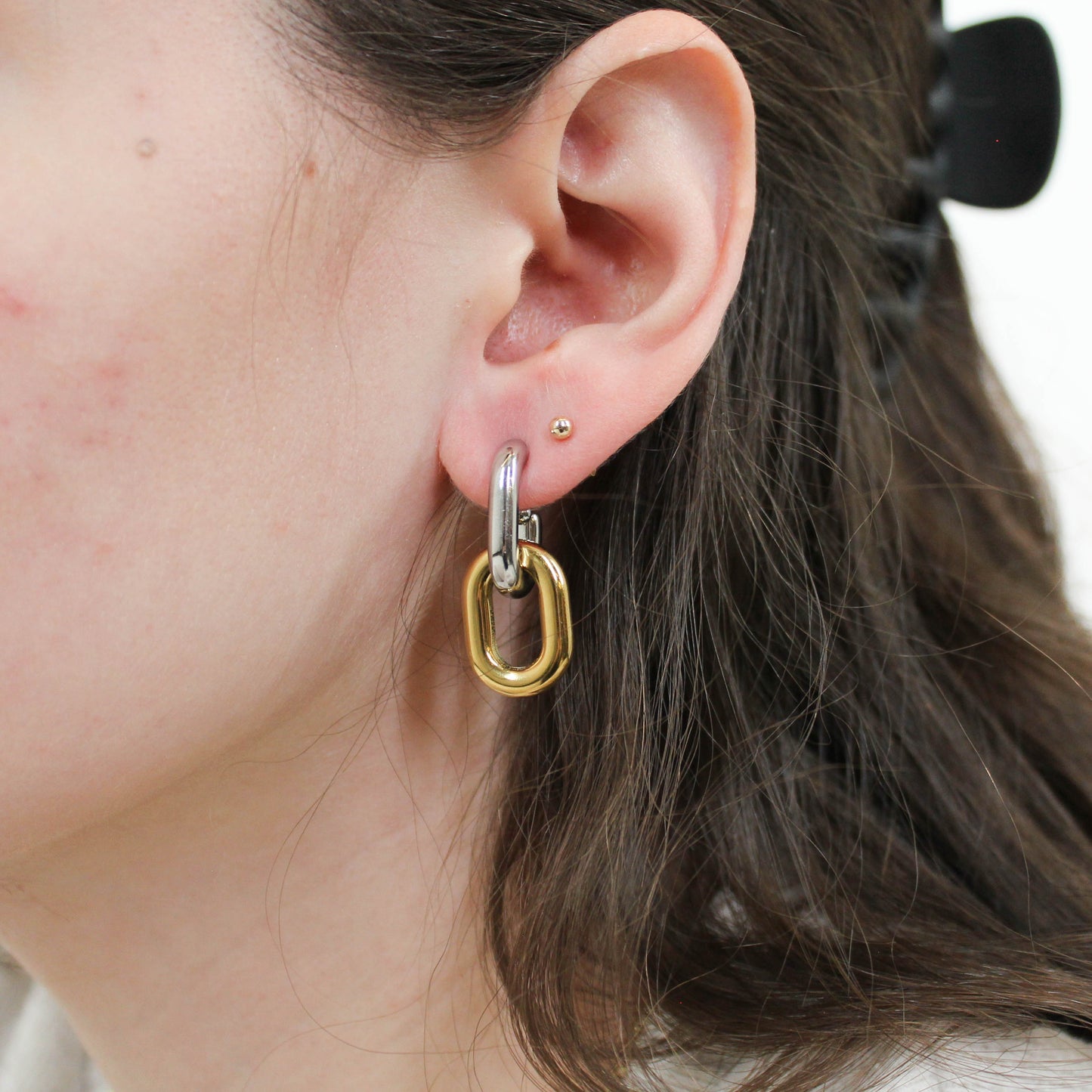 Close-up of an ear wearing a gold and silver mixed metal chain drop hoop earring.