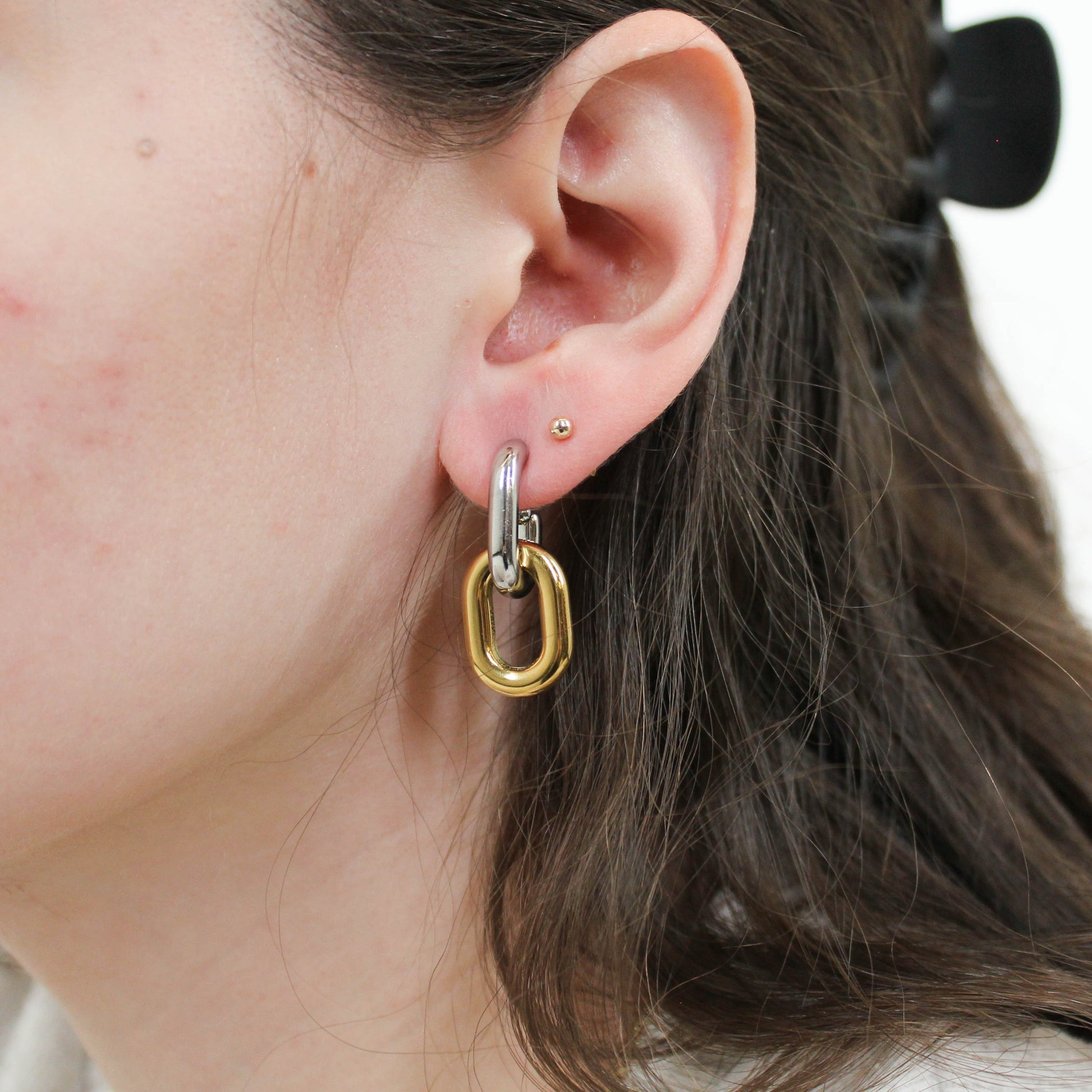 Close-up of an ear wearing a gold and silver mixed metal chain drop hoop earring.