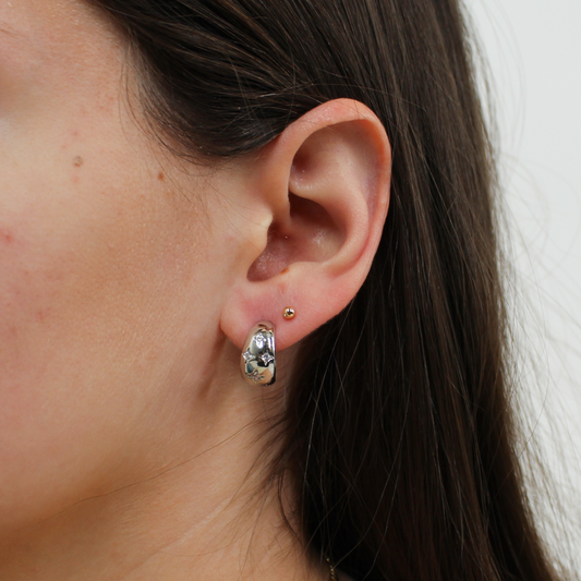 Close-up of an ear wearing a silver northern star hoop earring with a star design.