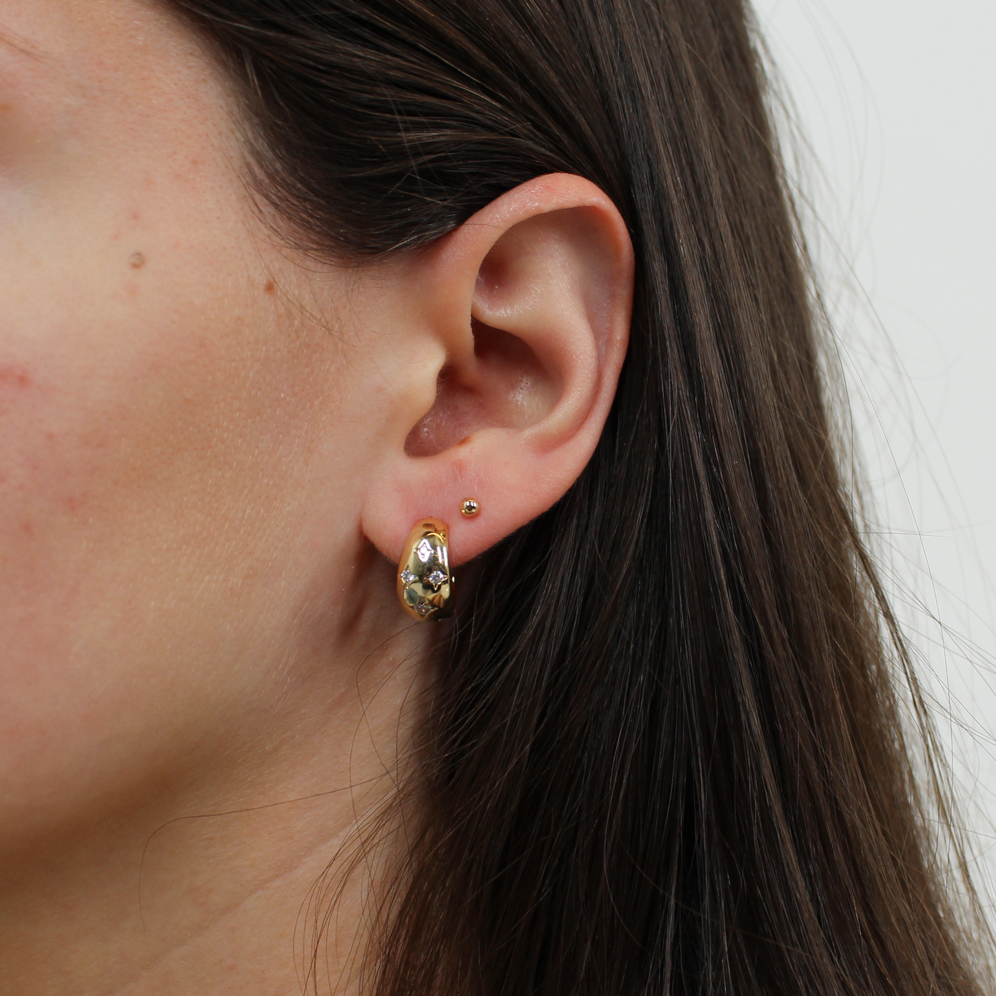 Close-up of an ear with gold northern starts hoop earrings against a neutral background
