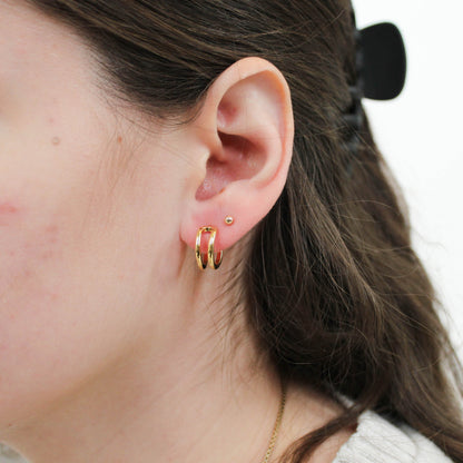 Close-up of a person wearing gold open mini hoop earrings with a neutral background