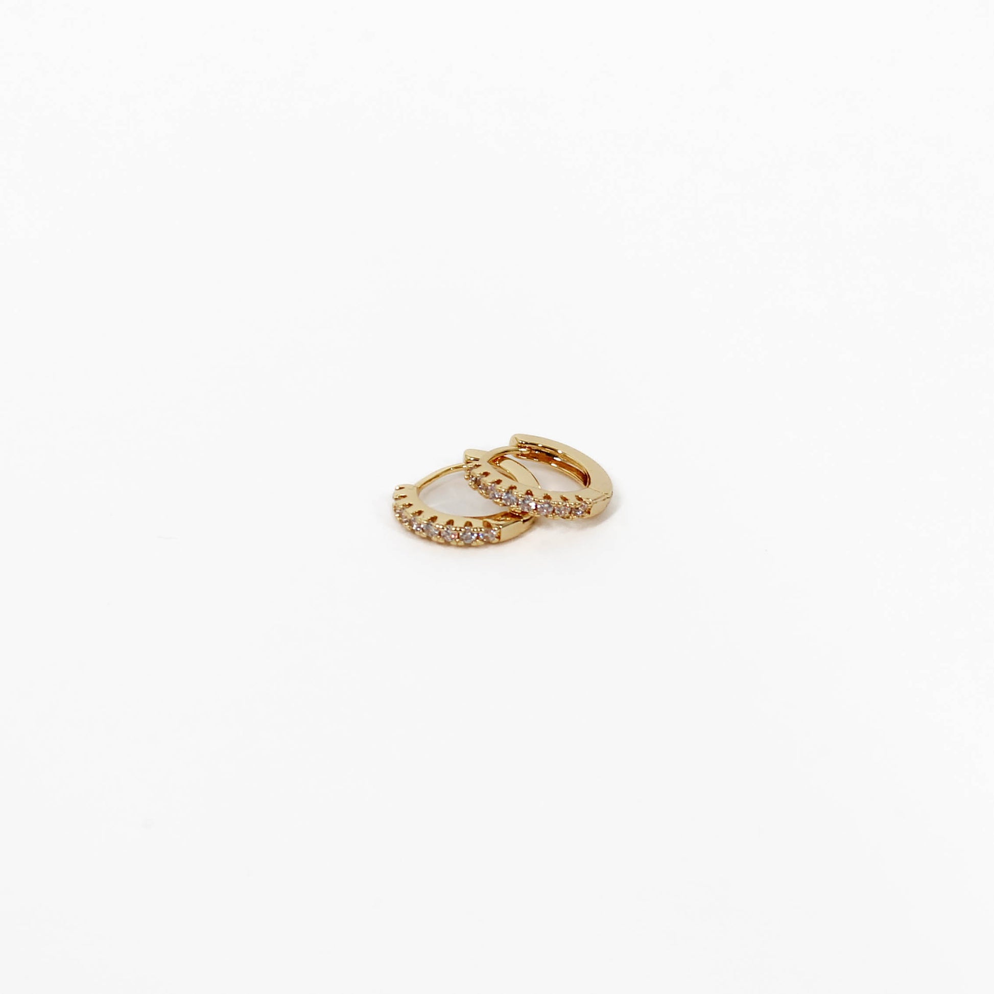 Gold hoop pave huggie earrings with small diamonds on a white background