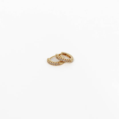 Gold hoop pave huggie earrings with small diamonds on a white background