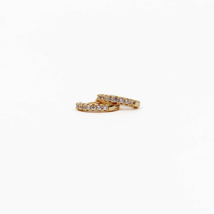 Two gold pave huggie earrings with diamond accents on a white background