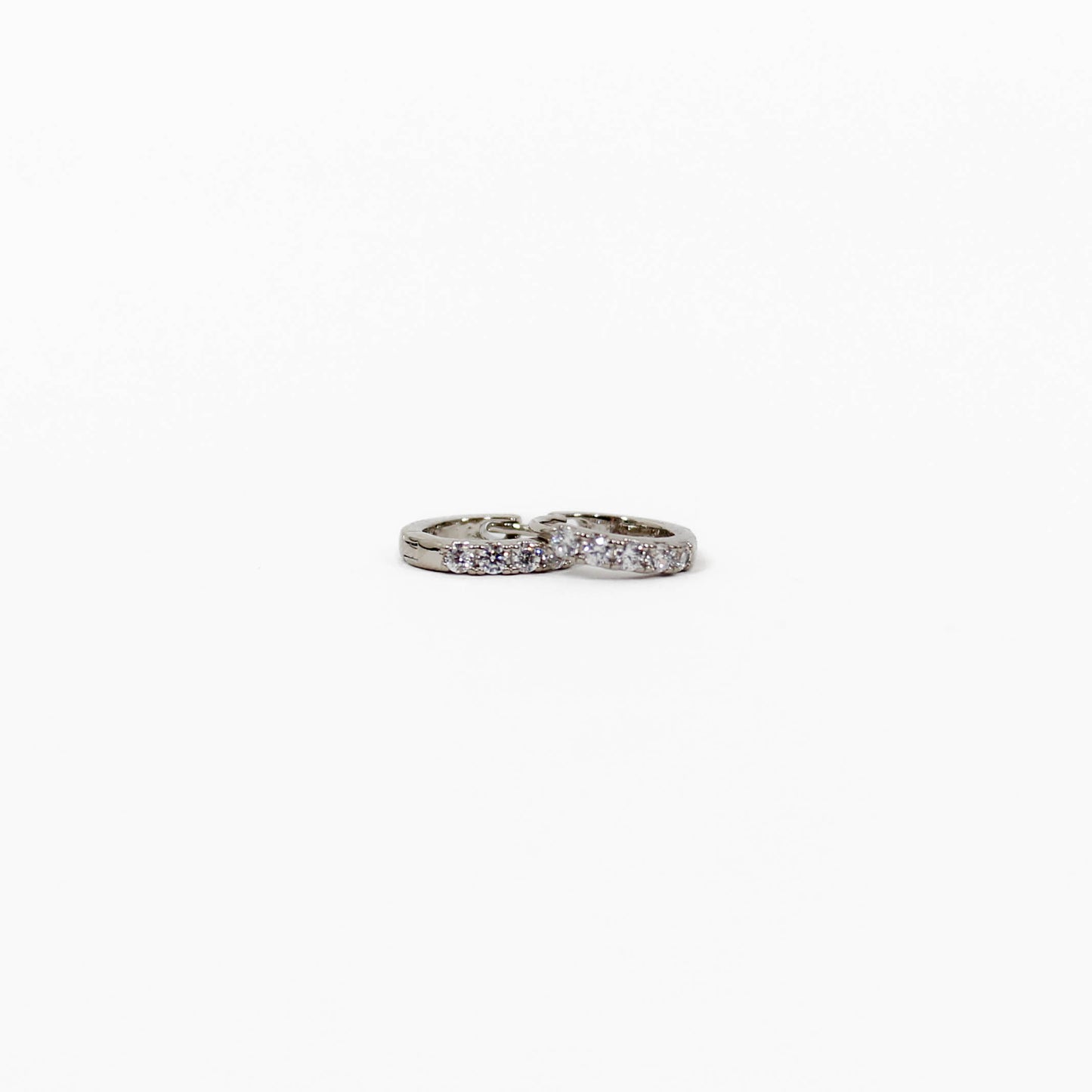 Silver pave huggie earrings with embedded stones on a white background