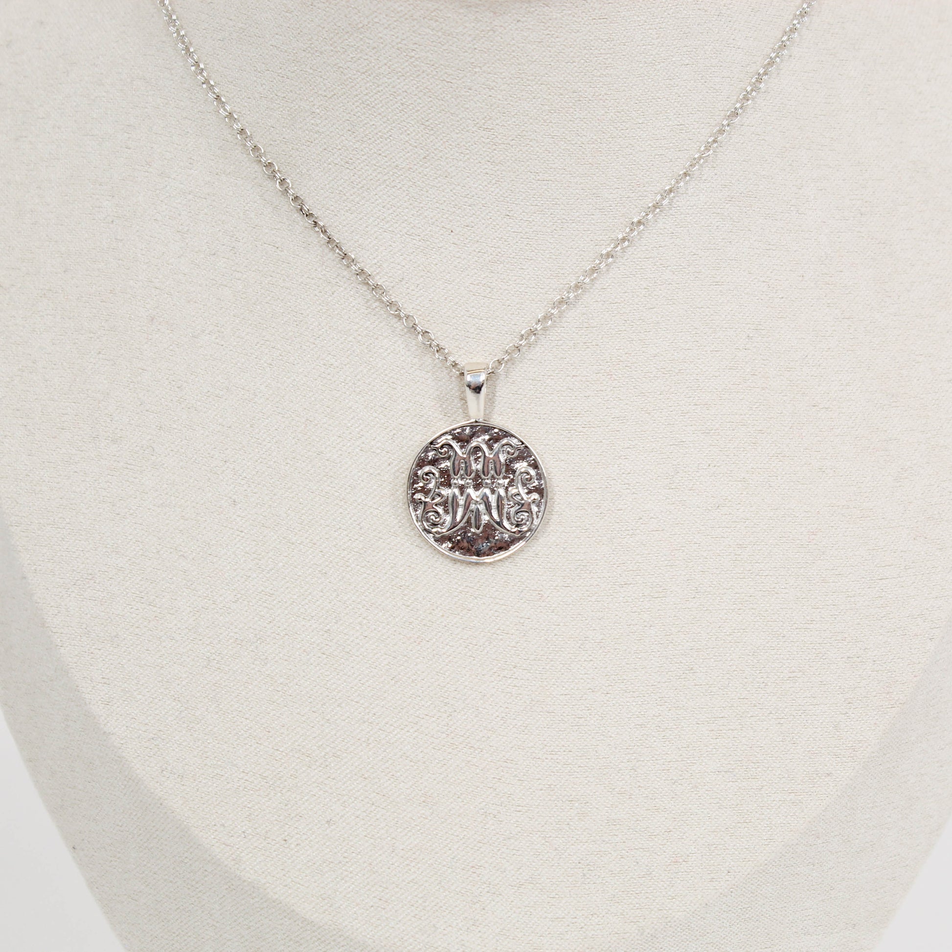 Silver scripted M Disc necklace for Marist on a white mannequin bust