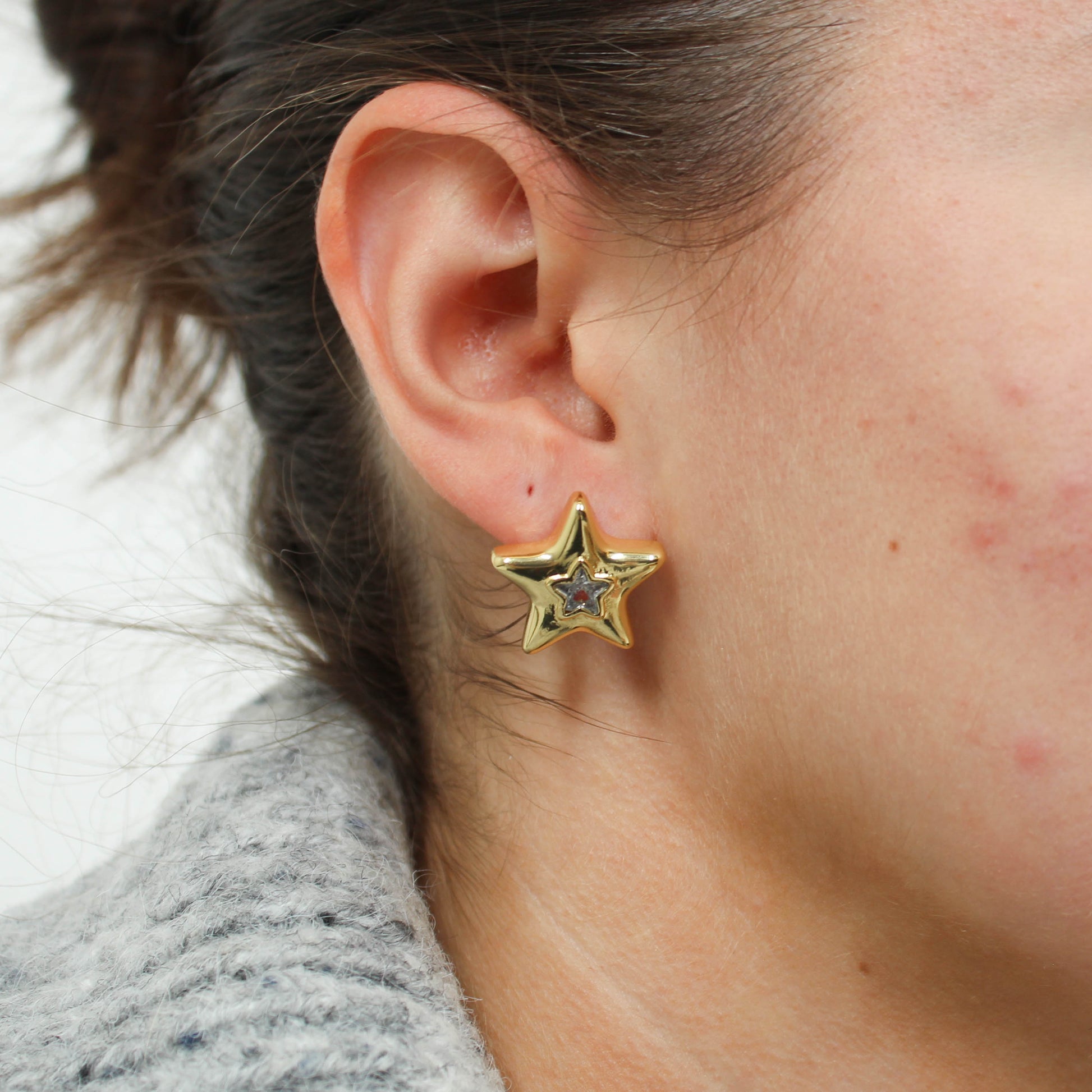 Gold star-shaped statement earring worn by a person with a neutral background