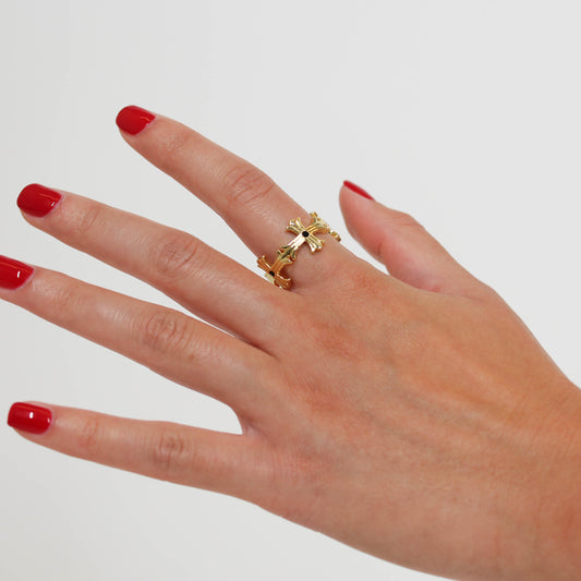 Hand wearing a gold ring with a cross design on a plain background