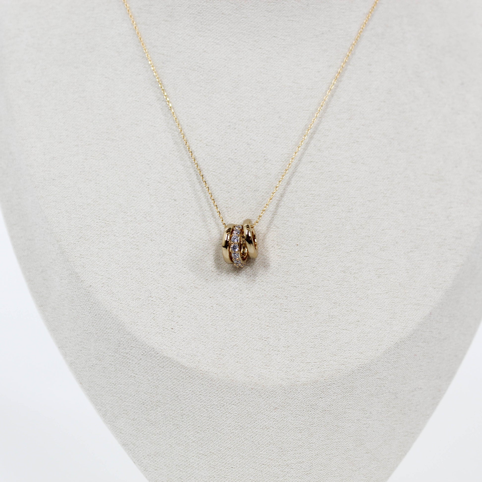 Gold three ring pendant necklace on a light gray stand