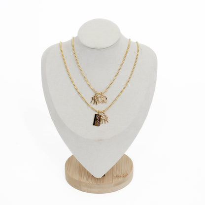 Two gold yankee charm pendant necklaces with metro card and pretzel charms on a white mannequin bust with a wooden base.