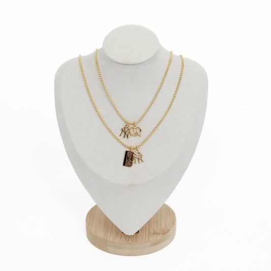 Two gold yankee charm pendant necklaces with metro card and pretzel charms on a white mannequin bust with a wooden base.