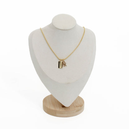 Gold yankee charm necklace with a metro card pendant on a white bust and wooden base against a white background