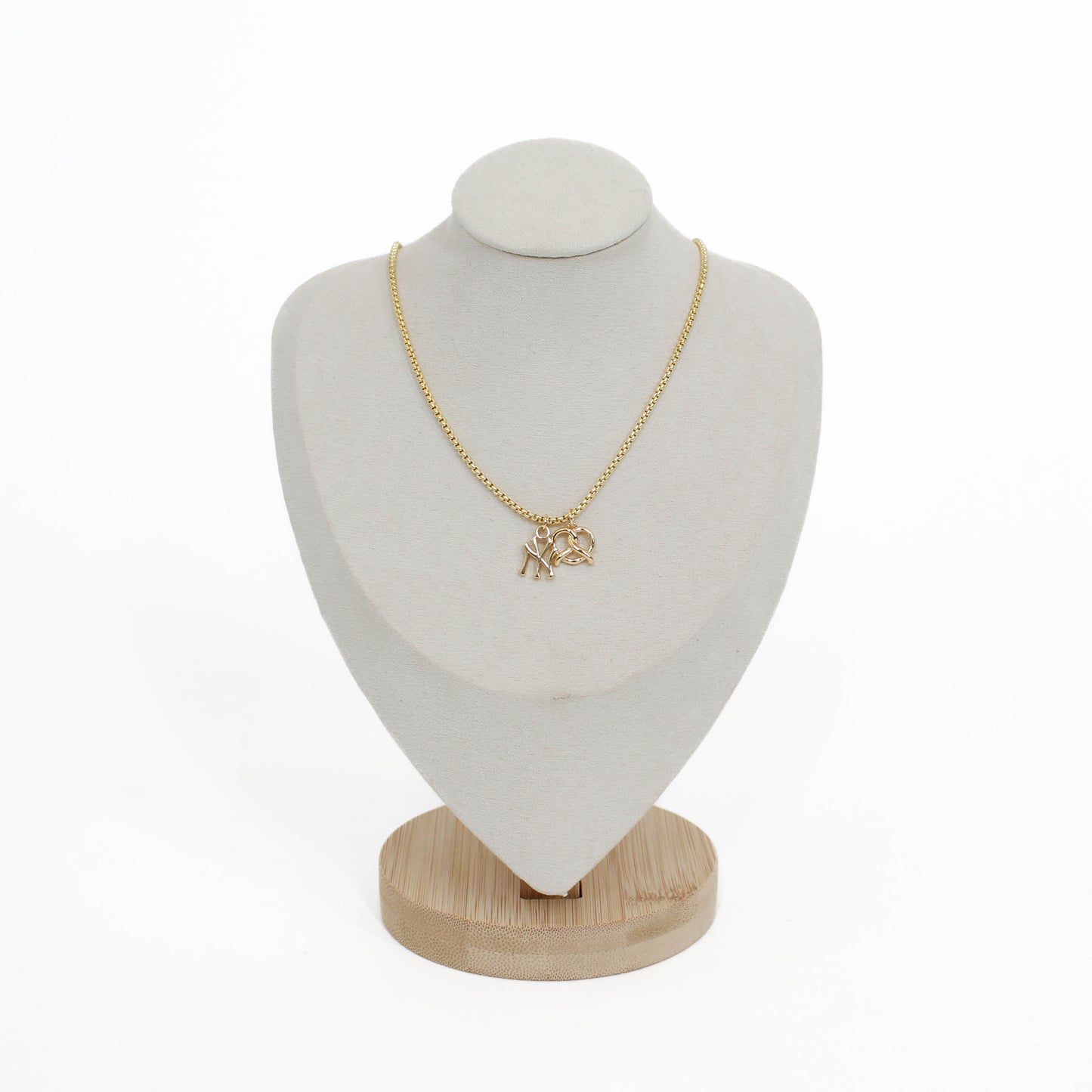 Gold yankee charm pendant necklace with a pretzel pendant on a white mannequin bust with a wooden base.