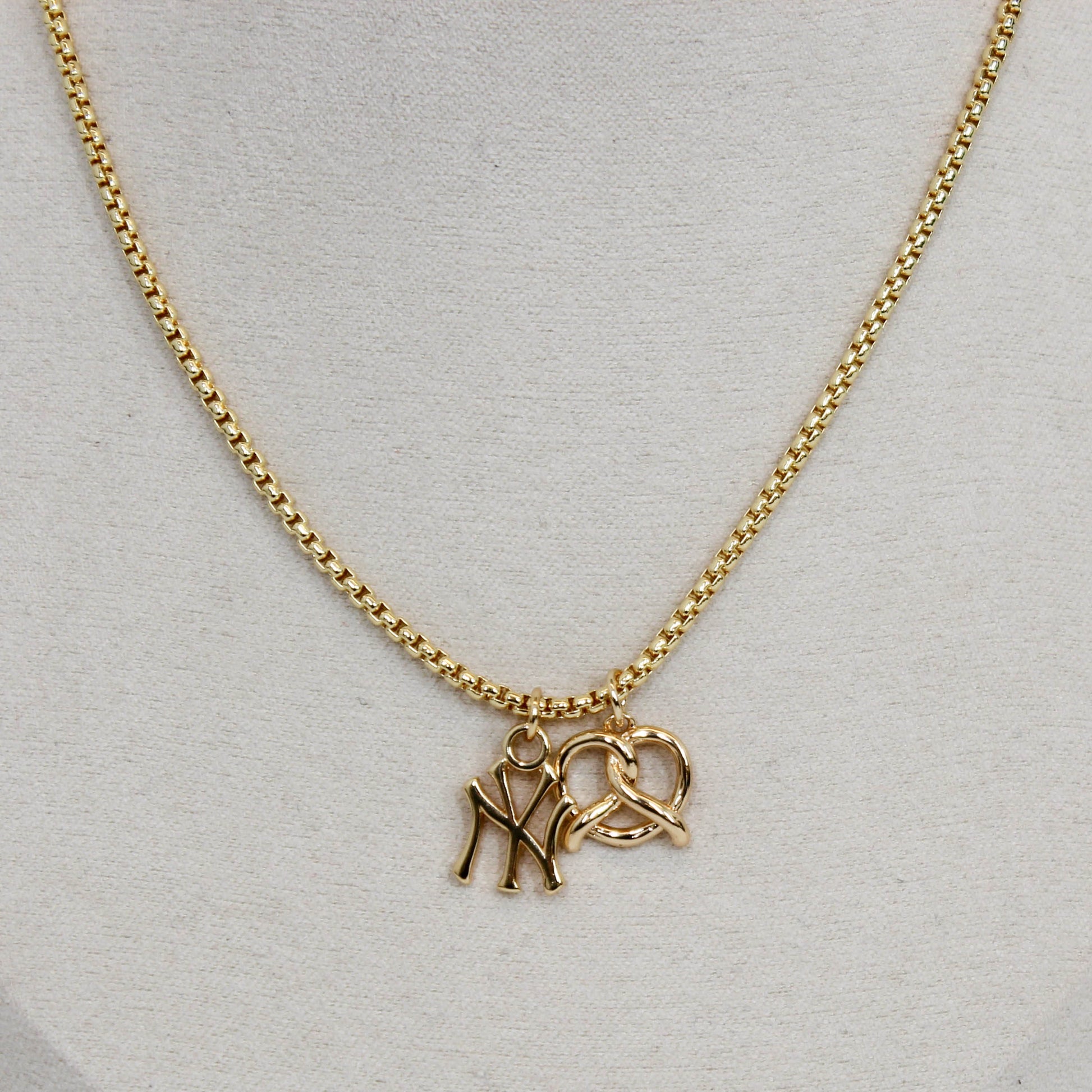 Gold yankee charm pendant necklace with a pretzel pendant on a light gray background