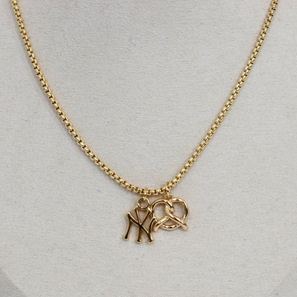 Gold yankee charm pendant necklace with a pretzel pendant on a light gray background