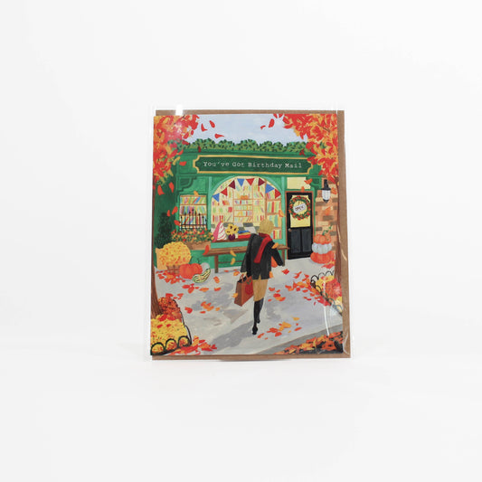 Greeting card with autumn-themed illustration of a person walking past a store named 'Your Old Birthday Mail'.