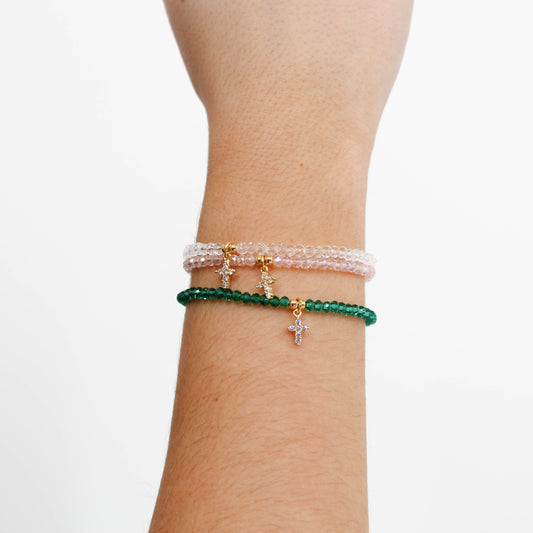 Three beaded cross charm bracelets on a wrist against a white background