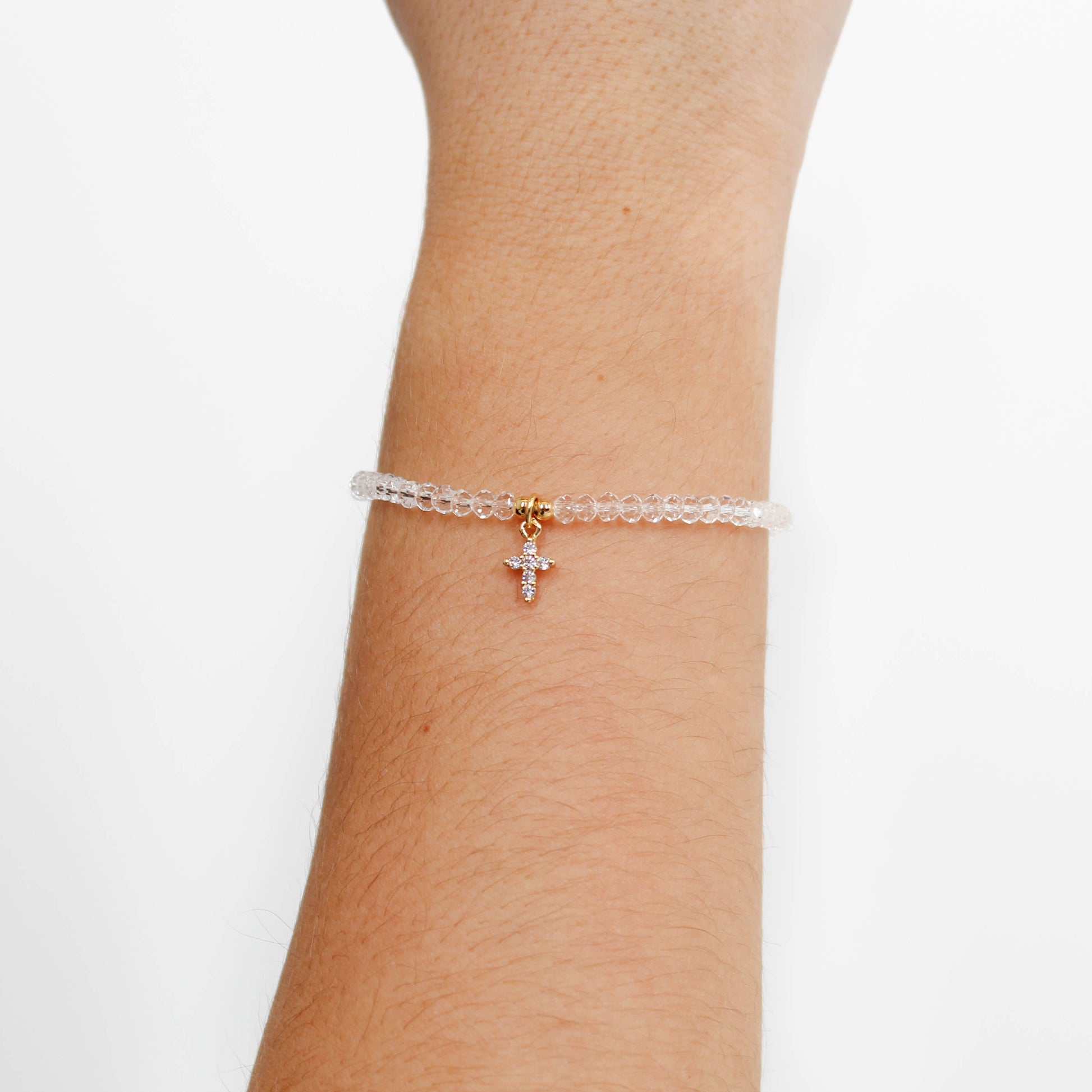 clear dainty cross charm bracelet with a cross charm on a wrist against a white background