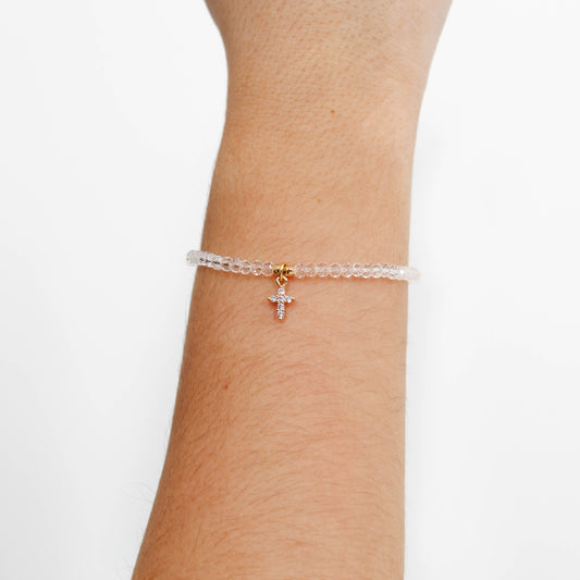 clear dainty cross charm bracelet with a cross charm on a wrist against a white background