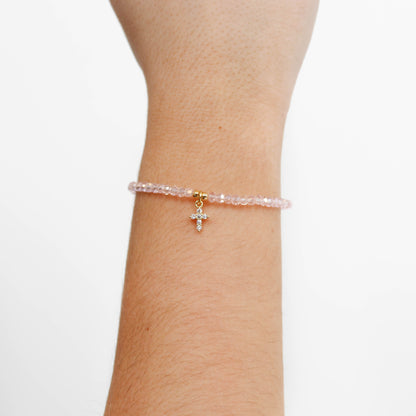 Pink beaded cross charm bracelet with a cross charm on a wrist against a white background