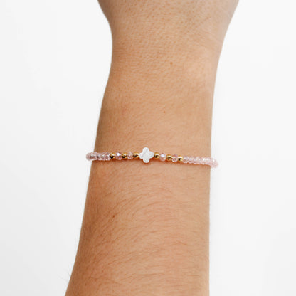 Close-up of a wrist wearing a delicate crystal clover bracelet with a clover-shaped clasp on a plain background