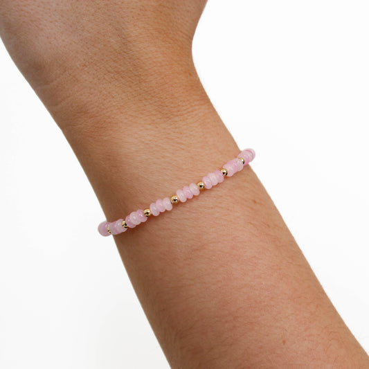 Pink and gold beaded dainty by sof bracelet on a wrist against a white background